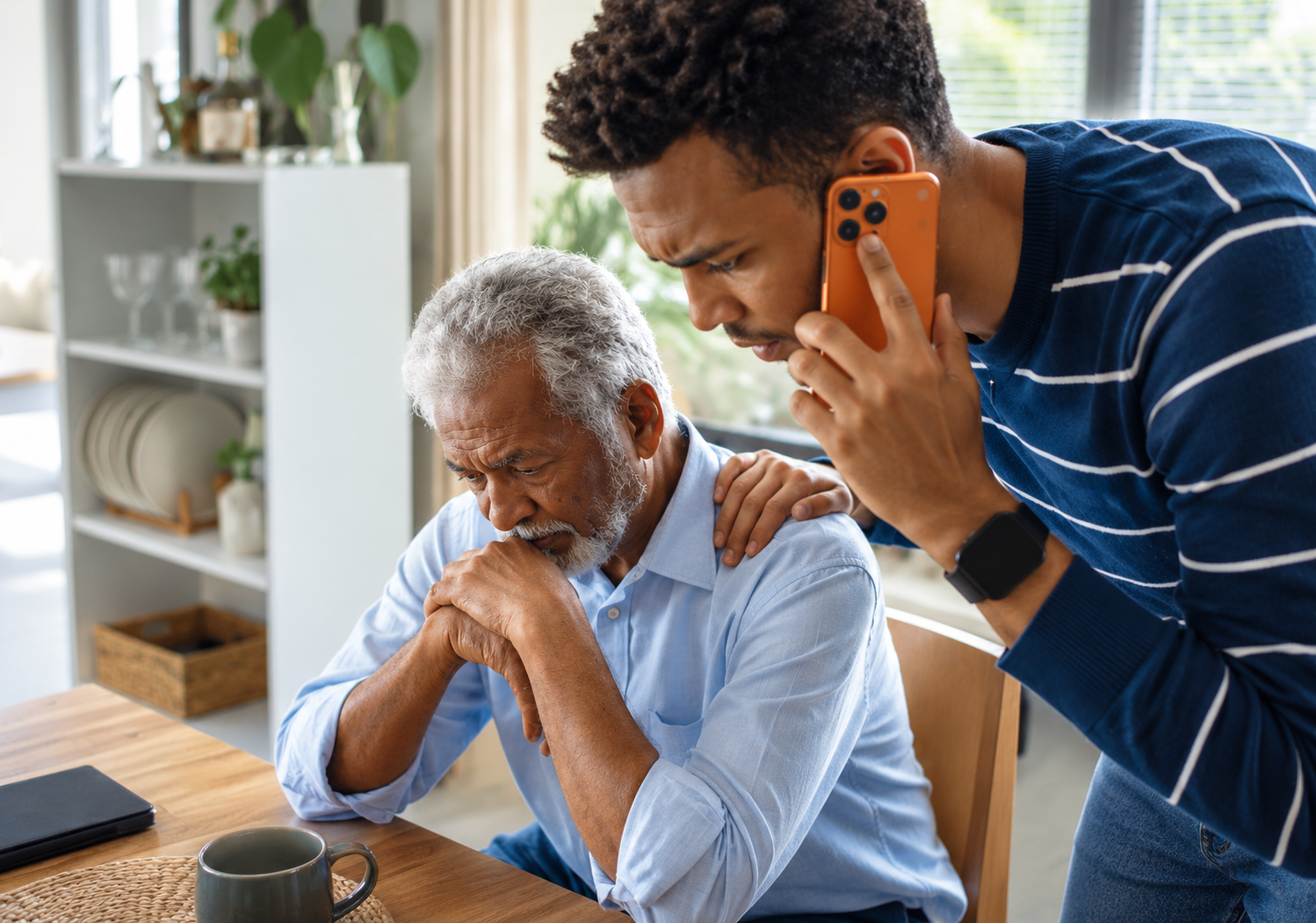 A concerned son calling for care support while comforting his father